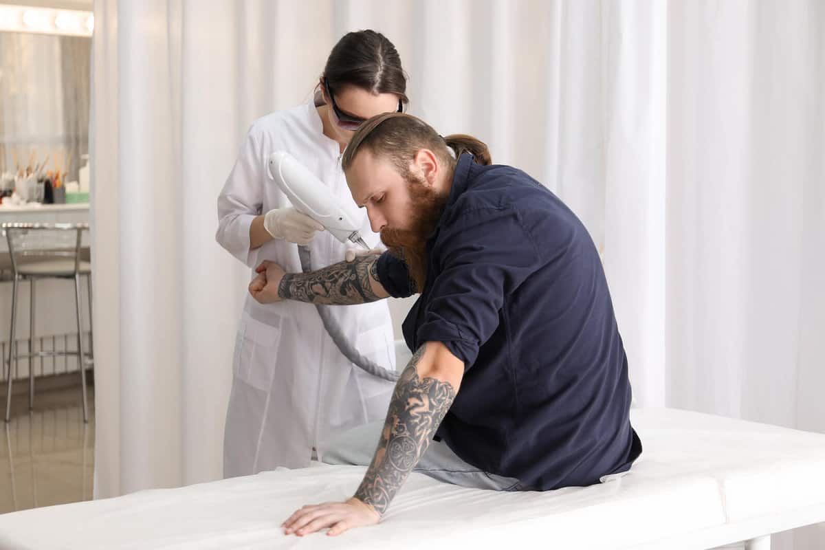 Man with tattoos getting laser tattoo removal sitting on a clinic bed