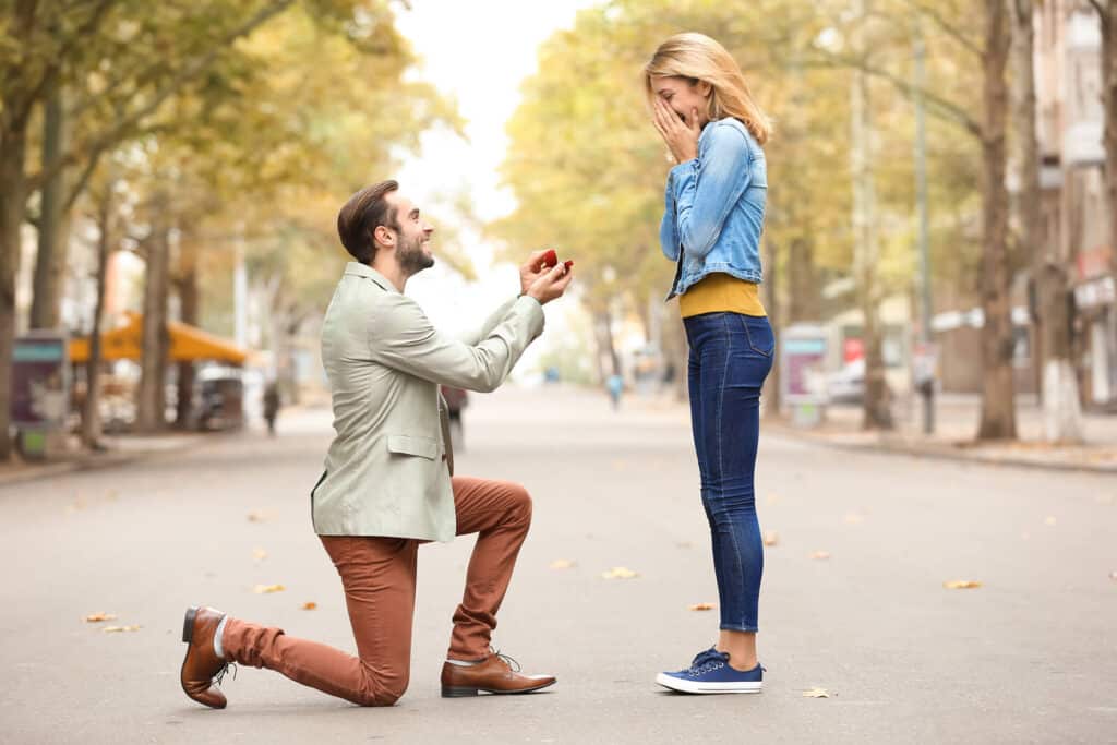 Man on one knee proposing to a woman in a public place