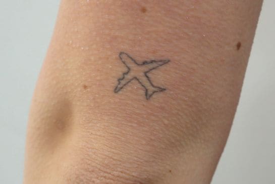 Showing small airplane outline tattoo near the elbow with fine black linework and minimalist styling.
